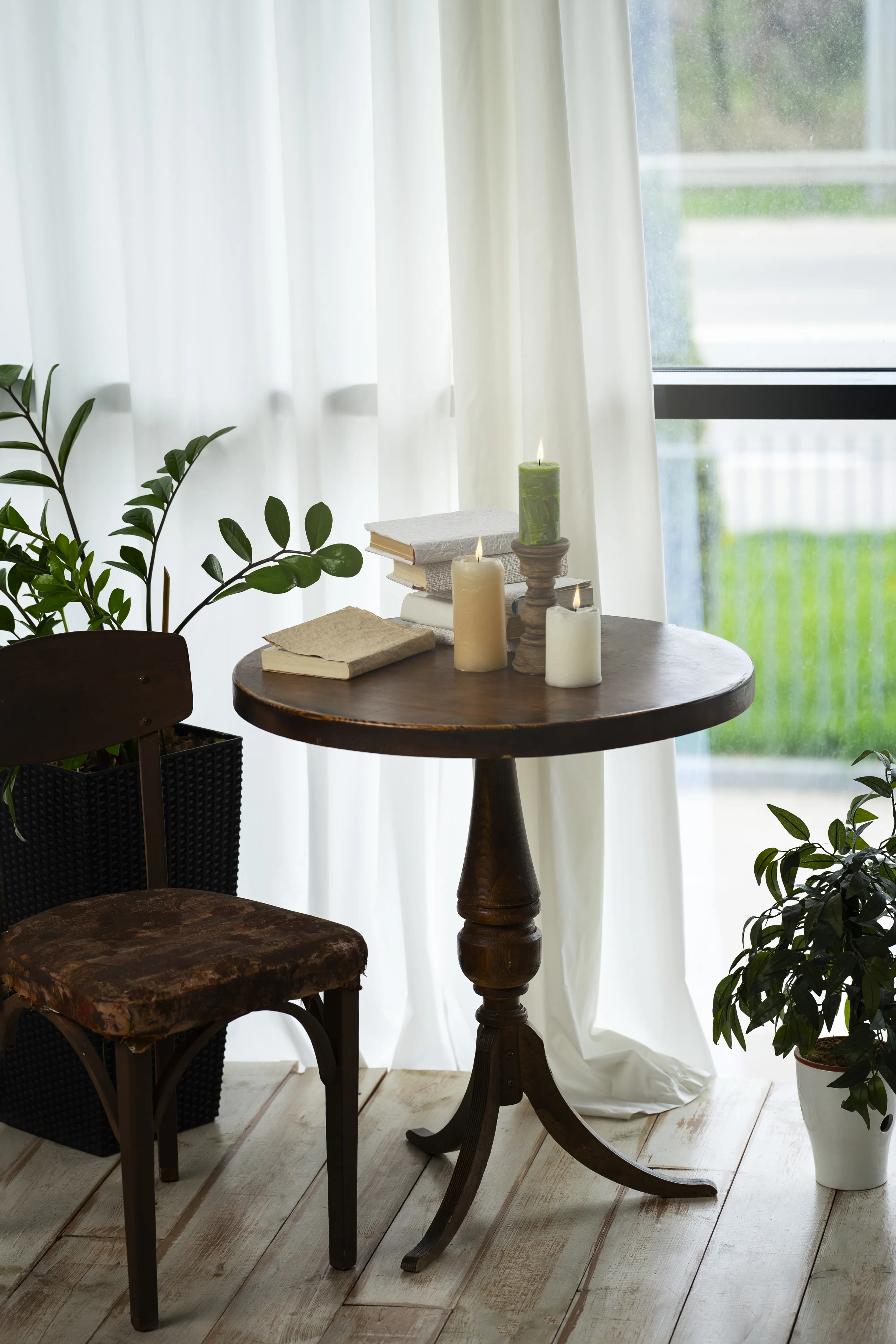 Cozy nook with a rustic wooden table, candles, books, and a vintage chair, surrounded by greenery and soft natural light.